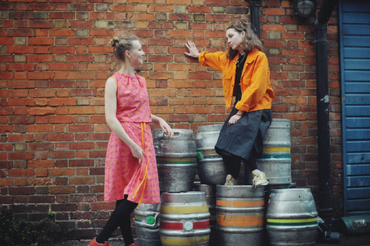 Young white women pose in Dorcas dresses on a pile of beer barrels