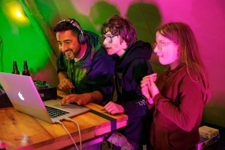 young people and adult DJ on laptop in tent, coloured lights
