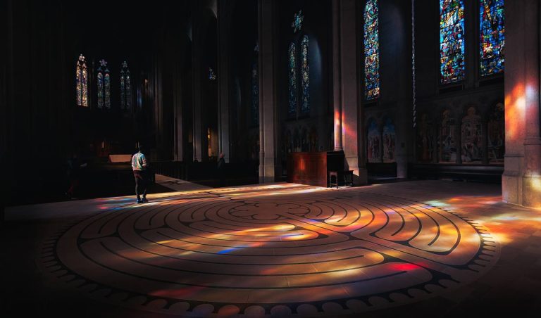 someone walks towards the edge of a labyrinth in cathedral bathed in stained glass light