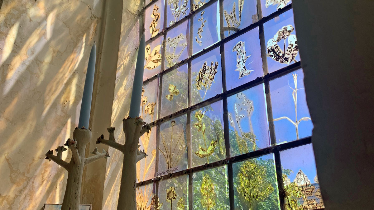 'tree' candlesticks silhouetted against a window, blue sky, with fossil-like flora on glass panes
