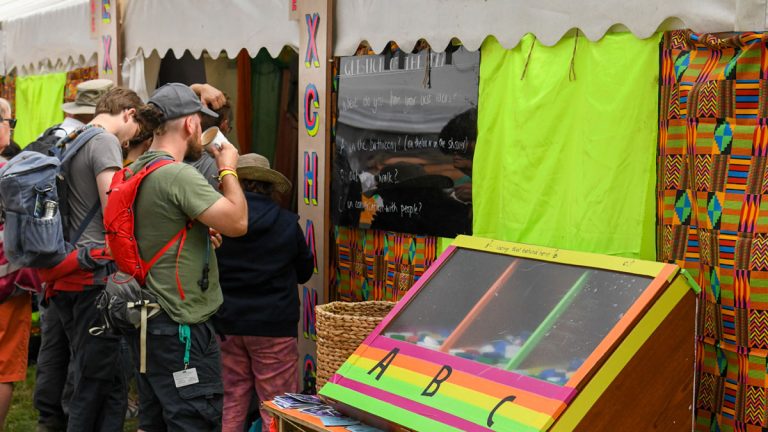 festivalgoers peer in to a crowded and birghtly decorated Exchange venue at Greenbelt Festival